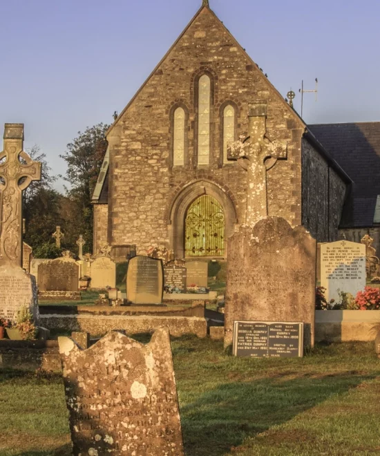 In the early morning light, Dunhill Old Church stands serenely amid a lush churchyard on the Copper Coast. Its arched windows and weathered gravestones add timeless charm, enveloping the scene in a profound sense of calmness.